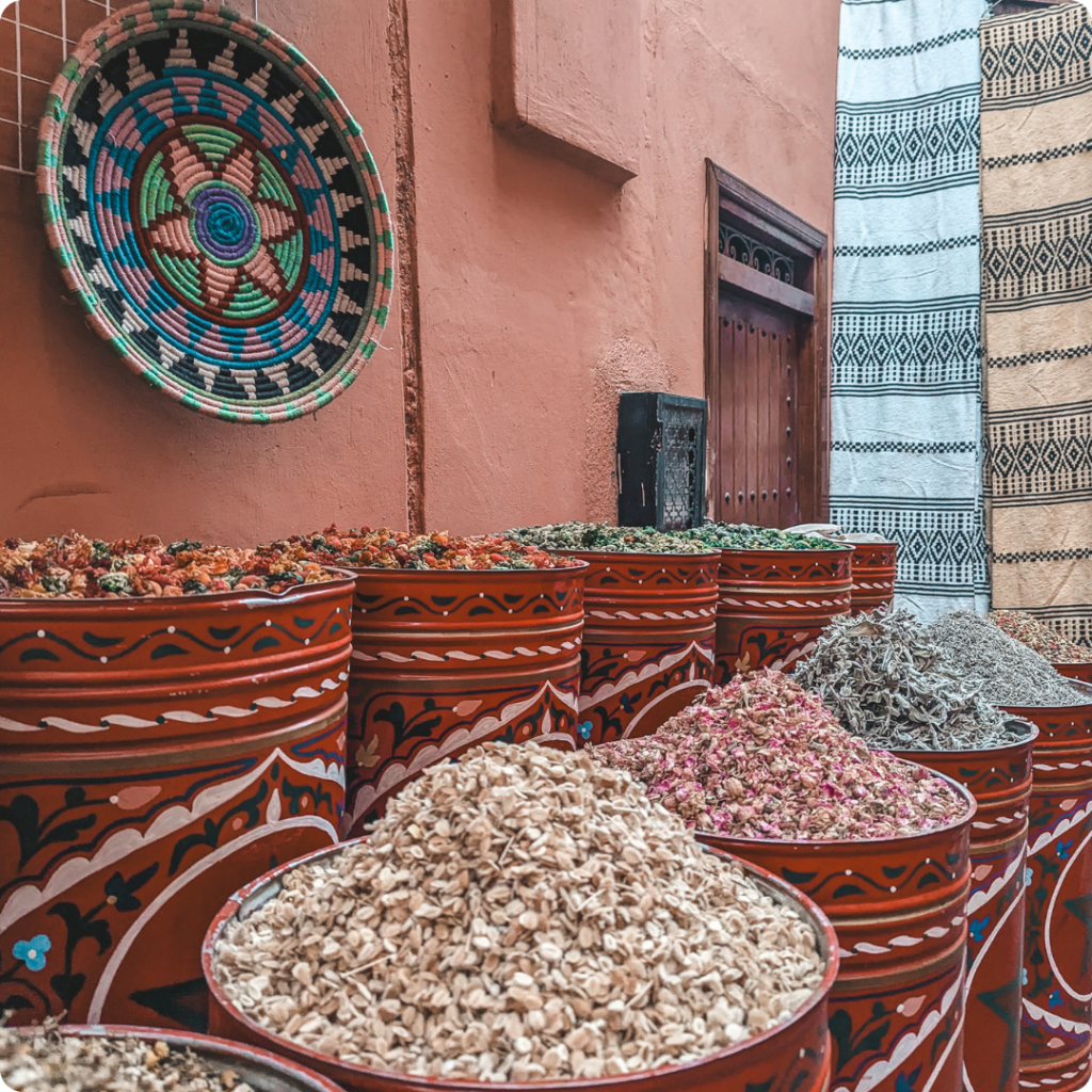 Vibrant display of Moroccan spices and dried herbs in a traditional souk, with hand-painted barrels and woven Berber décor—ideal for travel advisors showcasing Morocco’s sensory-rich markets, cultural immersion, and authentic culinary experiences.